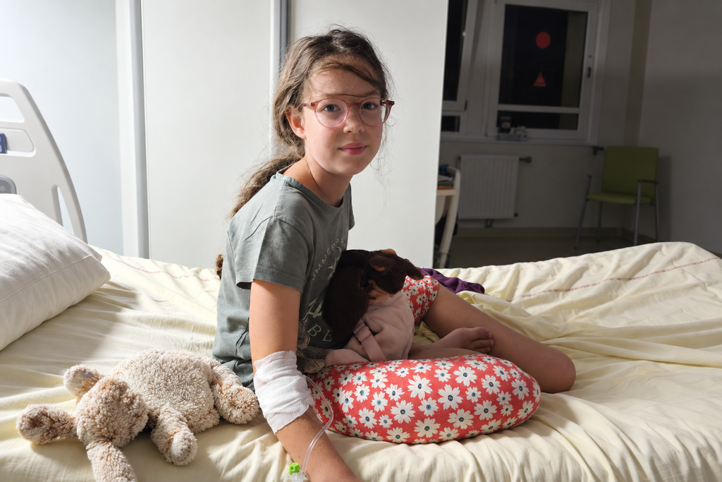 Jeune fille assise sur son lit d’hôpital avec sa peluche pendant une hospitalisation.
